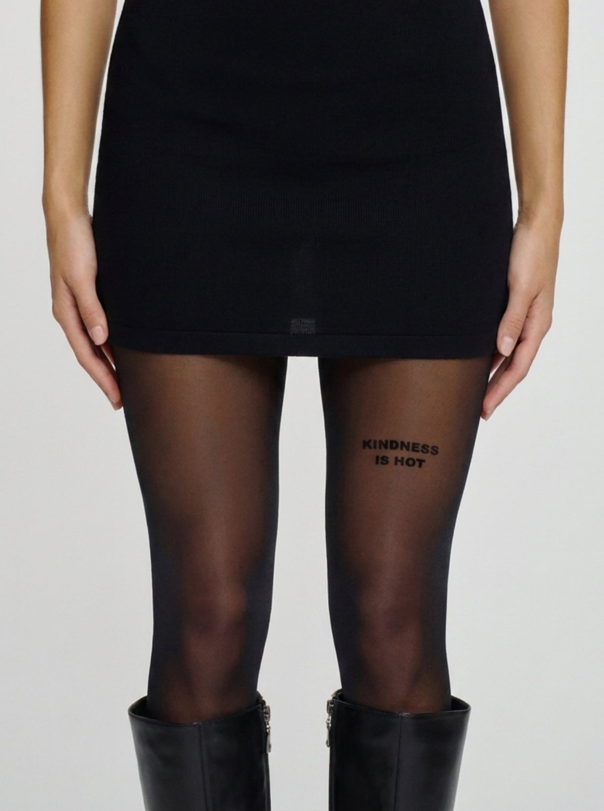 Model trägt schwarze Statement-Strumpfhose mit „KINDNESS IS HOT“-Schriftzug am Oberschenkel.