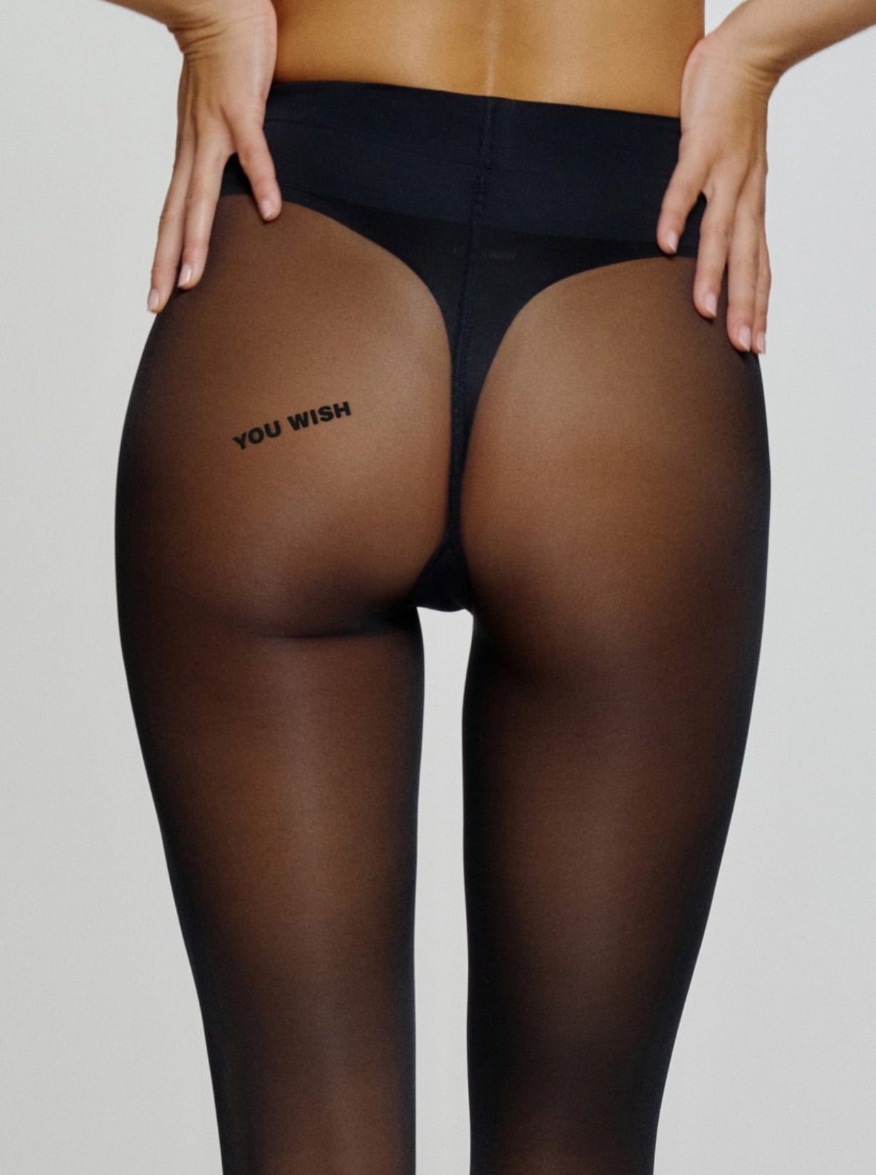 Model trägt schwarze Statement-Strumpfhose mit „YOU WISH“-Schriftzug auf der Rückseite.
