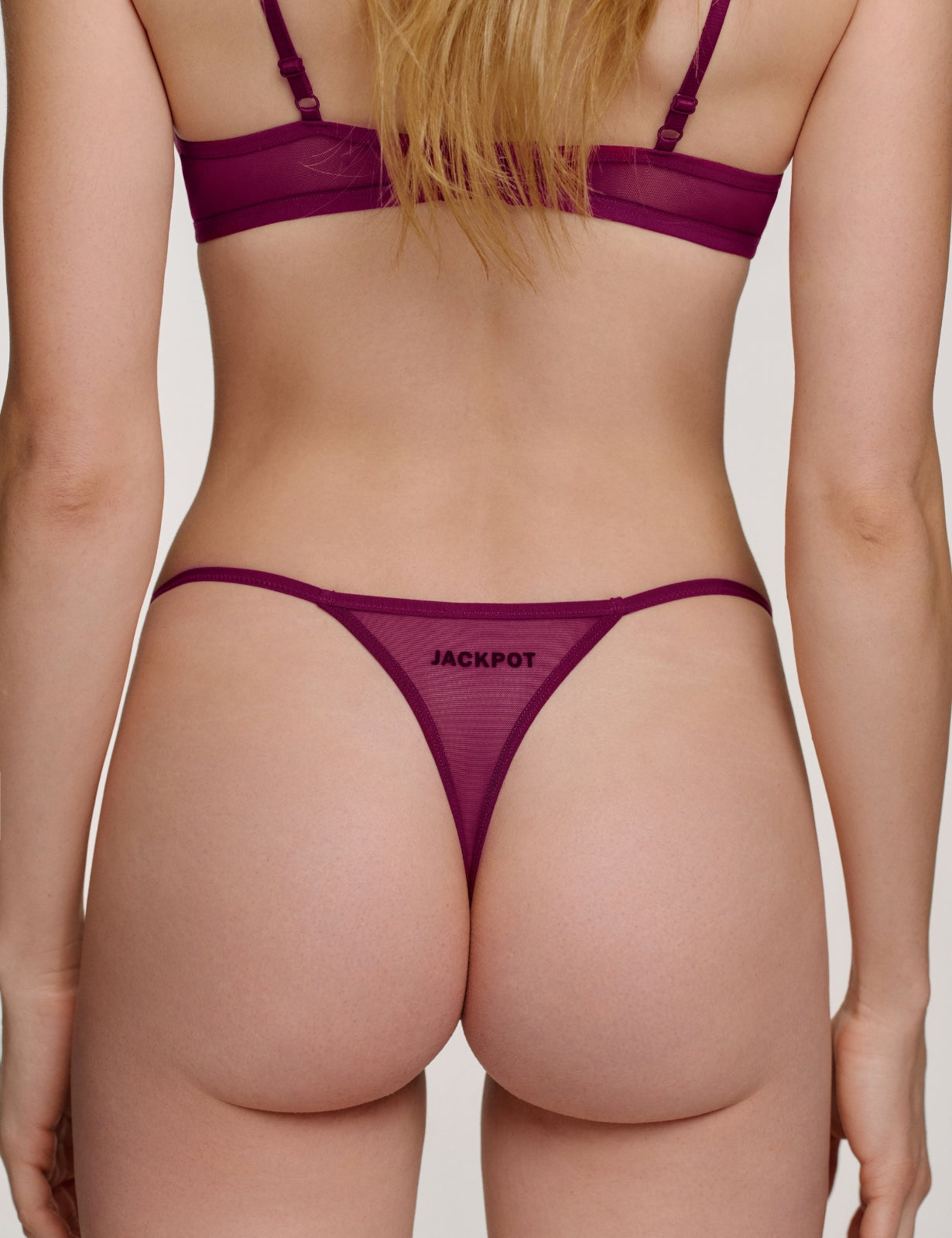 Rückansicht des Saint Sass Jackpot Tanga in Plum Red, elastischer Bund, vor neutralem Hintergrund.