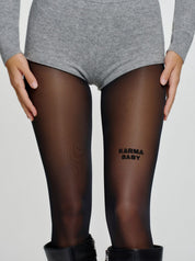 Model trägt schwarze Statement-Strumpfhose mit „KARMA BABY“-Schriftzug am Oberschenkel.