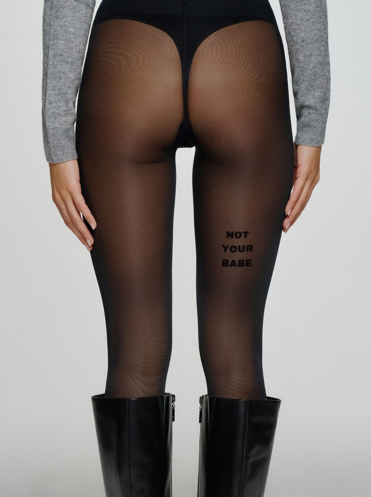 Model trägt schwarze Statement-Strumpfhose mit „NOT YOUR BABE“-Schriftzug auf der Rückseite des Oberschenkels.