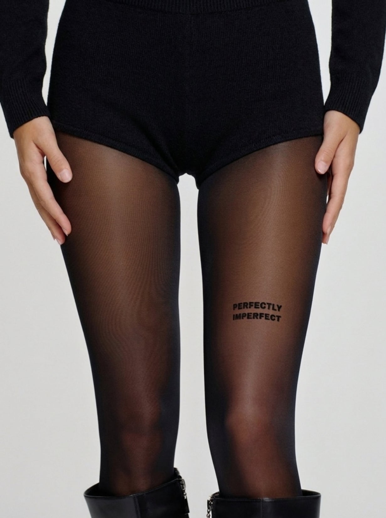 Model trägt schwarze Statement-Strumpfhose mit „PERFECTLY IMPERFECT“-Schriftzug am Oberschenkel.