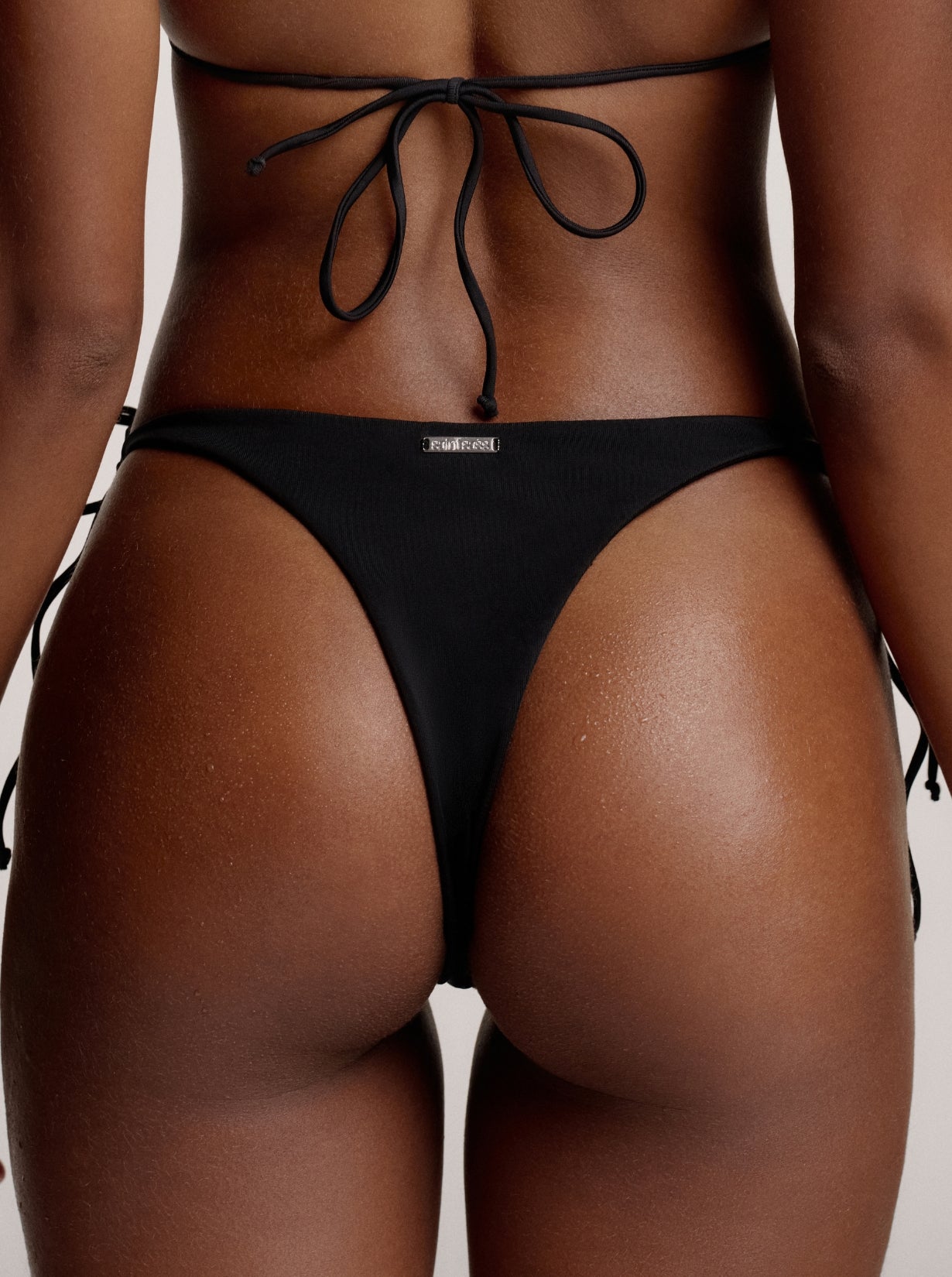 Rückansicht von schwarzen Chloe Bikini Bottoms mit silbernen saint sass Metalllogo in der Mitte oben