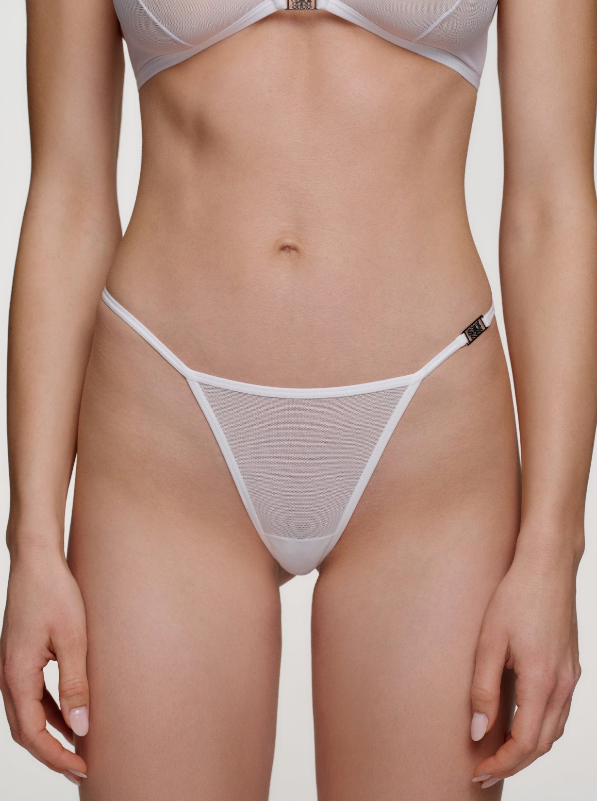 Model trägt Saint Sass Gigi Mesh Tanga in Weiß, Vorderansicht, vor neutralem Hintergrund.