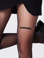 Detailaufnahme der schwarzen Statement-Strumpfhose mit Aufdruck SHOWGIRL am Oberschenkel – Saint Sass“